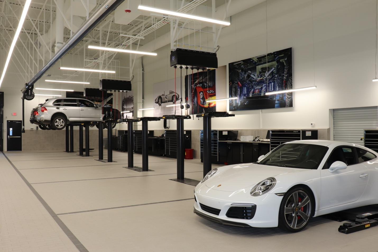 A white sports car sits on the ground of a high-end service center. Four more bays sit next to it with in-ground lifts.