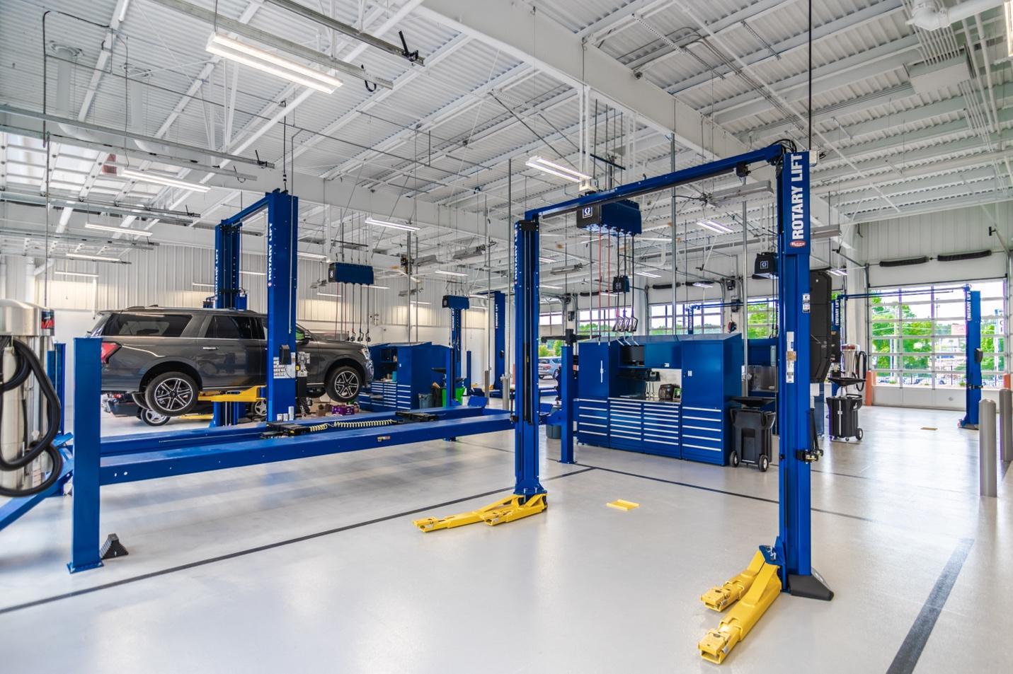 A blue two-post automotive lift is sitting in a service center. An alignment and heavy-duty two-post lift are next to it.