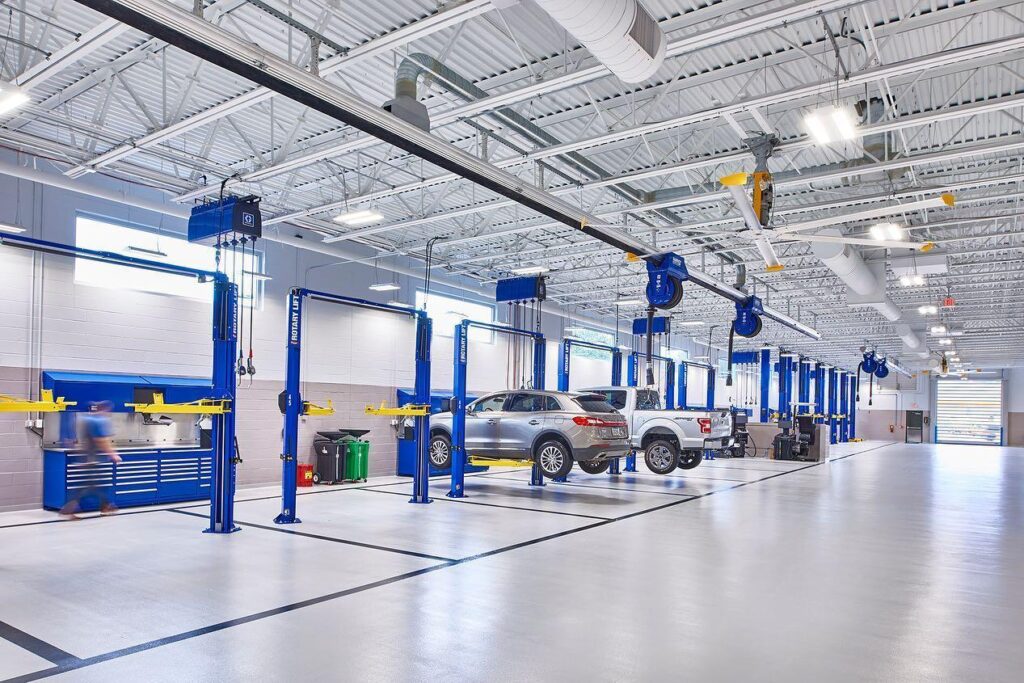 The interior of a modern automotive service center. Six blue two-post lifts are set up to optimize the fixed ops layout.