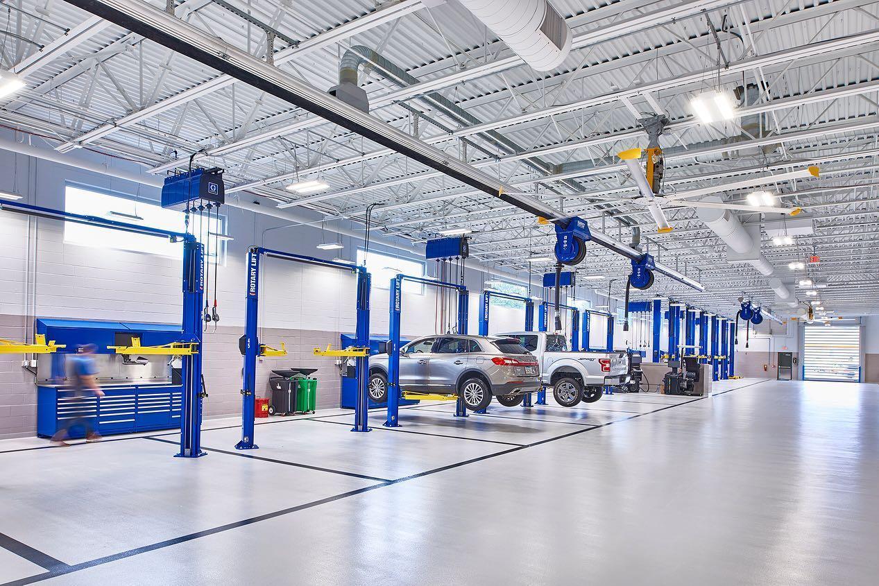 The interior of a modern automotive service center. Six blue two-post lifts are set up to optimize the fixed ops layout.